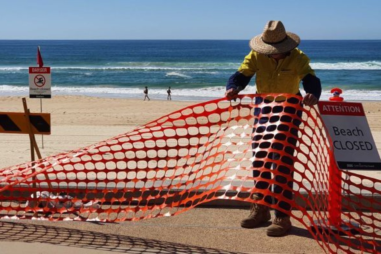 A council worker removes barriers installed at Surfers Paradise on the Gold Coast. However the State's border restrictions remain in place, despite industry pleas. Photo: ABC