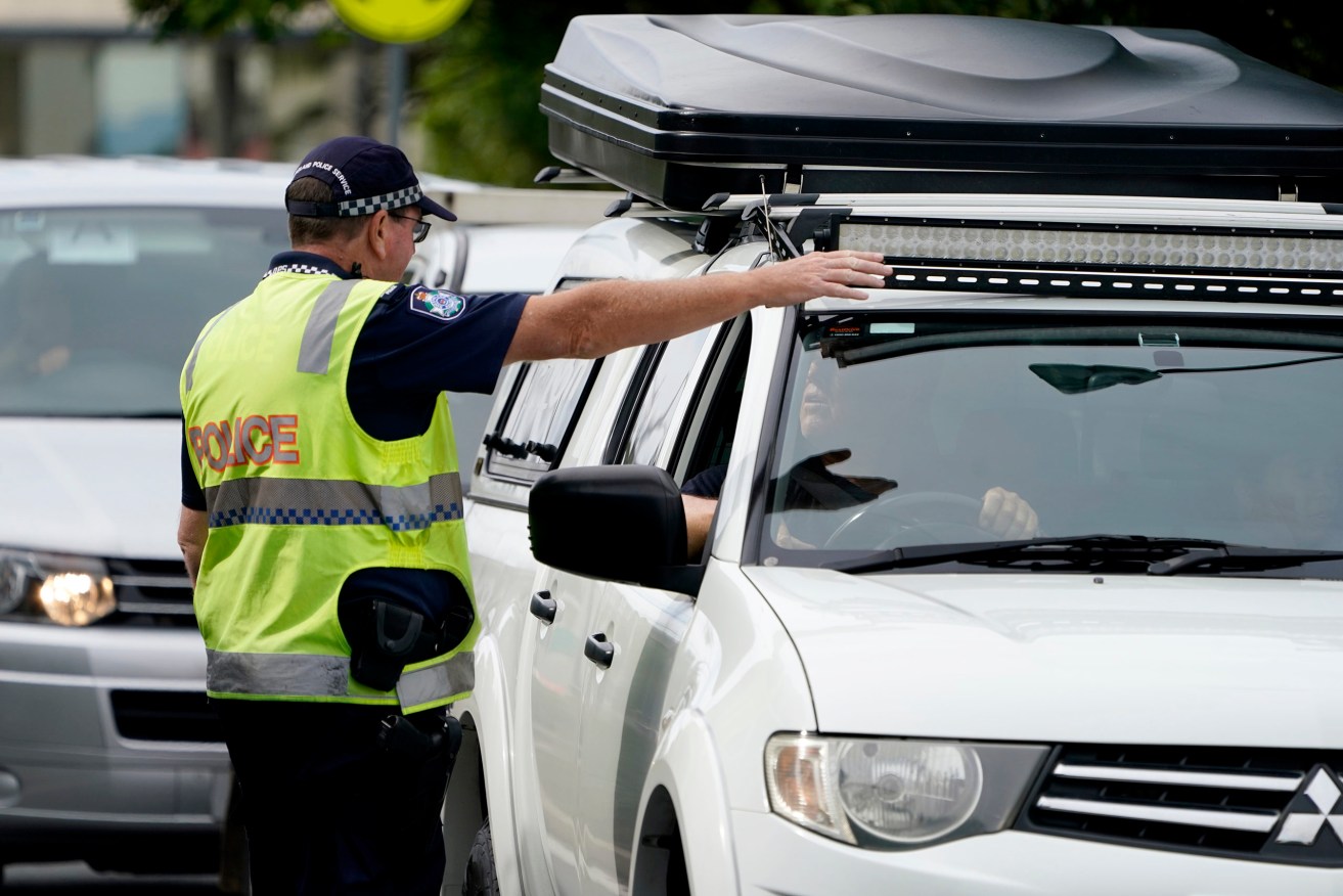 A Queensland police officer gestures for a motorist to pull over at a checkpoint at Coolangatta on the Queensland-New South Wales border. (Photo: AAP Image/Dave Hunt) 