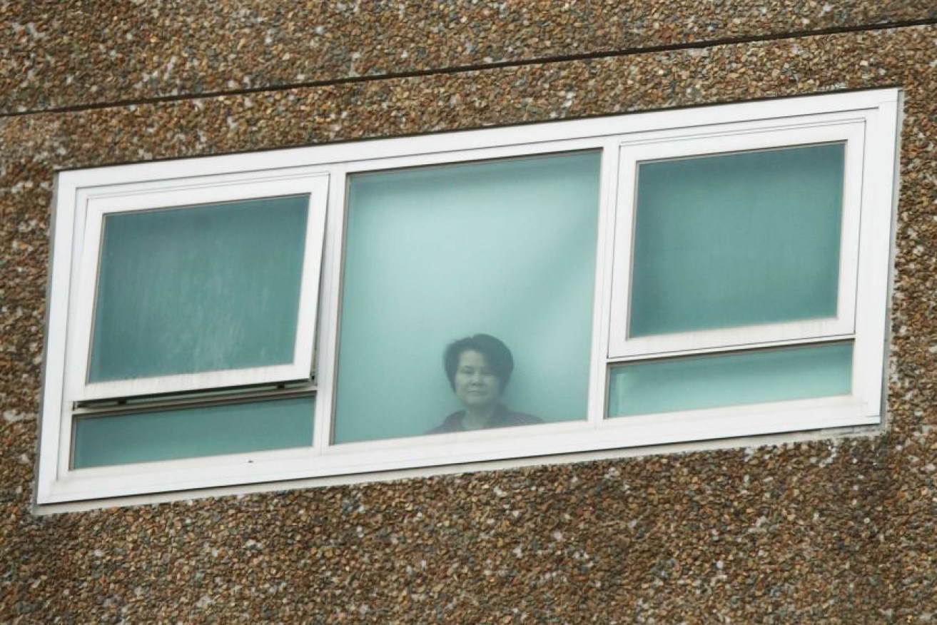 A resident peers out of her window on one of nine public housing apartment towers locked down in Melbourne. (ABC photo)