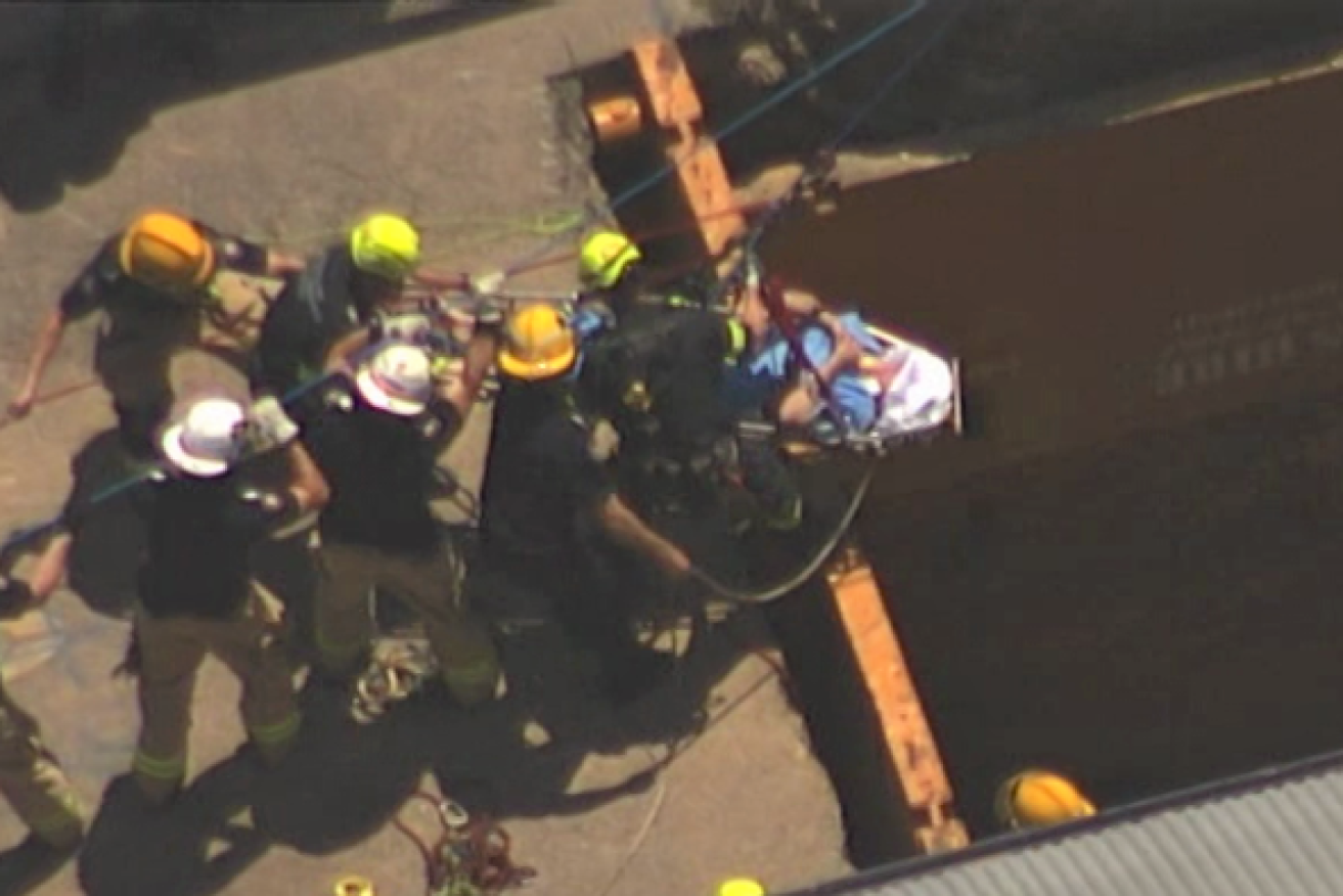 A man is winched to safety by firefighters after falling down a hole at a Brisbane building site. (Photo: ABC)