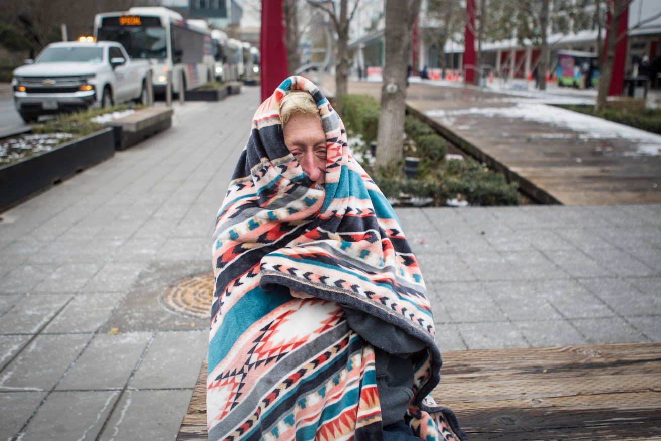 Michelle DeFord bundles up in a blanket to stay warm outside the warming shelter at the George R. Brown Convention Center, where she is staying during the frigid cold weather Tuesday, Feb. 16, 2021, in Houston. Temperatures stayed below freezing Tuesday. (Brett Coomer/Houston Chronicle via AP)
