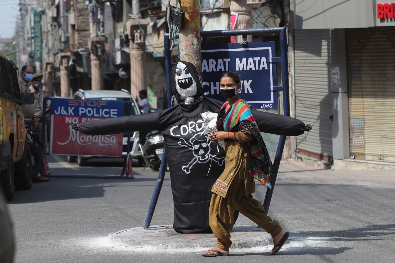A woman wearing a face mask walks past an effigy of coronavirus at a market in Jammu, India. (AP Photo/Channi Anand)