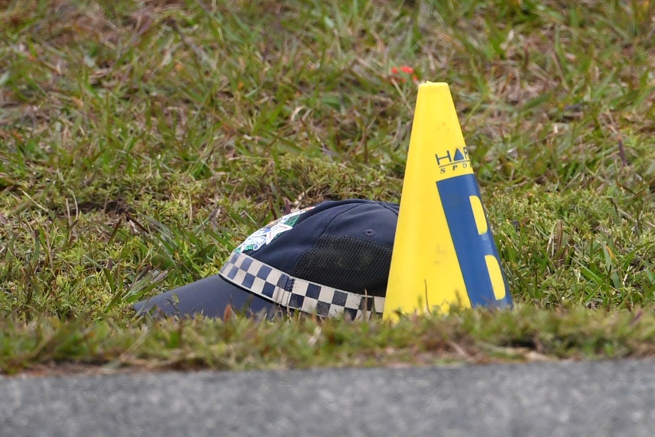 The police cap of 53-year-old Senior Constable David Masters is seen next to a evidence marker beside the Bruce Highway at Burpengary in Brisbane, Saturday, June 26, 2021. Senior Constable Masters was killed attempting to stop a suspected stolen car when deploying stingers or a tyre-deflating device just after 3am on the Bruce Highway. (AAP Image/Darren England) NO ARCHIVING