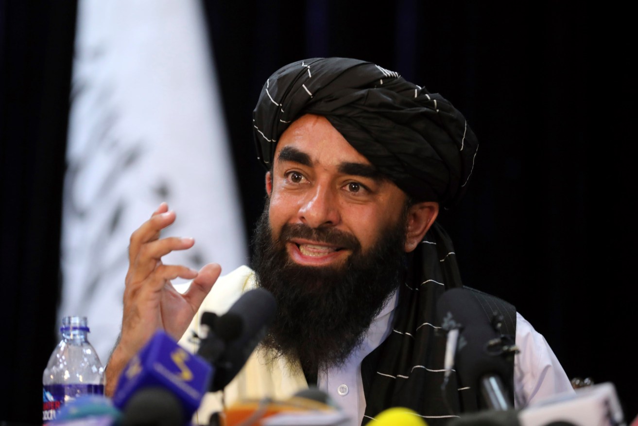 In front of a Taliban flag, Taliban spokesman Zabihullah Mujahid speaks at at his first news conference, in Kabul, Afghanistan, Tuesday. Mujahid vowed that the Taliban would respect women's rights, forgive those who resisted them and ensure a secure Afghanistan as part of a publicity blitz. (AP Photo/Rahmat Gul)