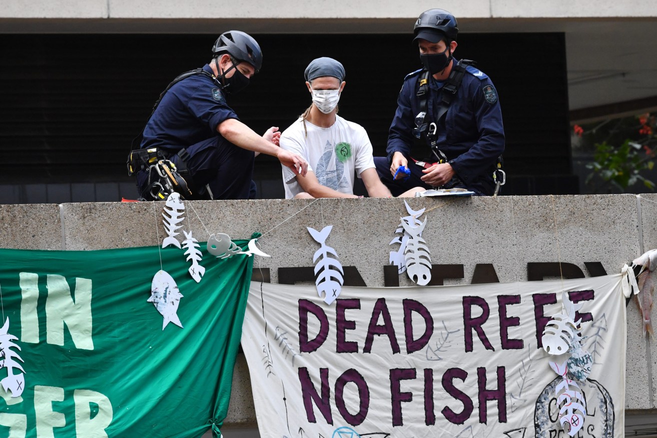 Police are seen detaining an Extinction Rebellion protestor (centre) on the roof of the parliamentary annexe at Queensland Parliament House in Brisbane, Wednesday, October 13, 2021. Queensland Parliament has been disrupted by Extinction Rebellion protestors after a protestor climbed onto the roof of the parliamentary annexe building. (AAP Image/Darren England) NO ARCHIVING