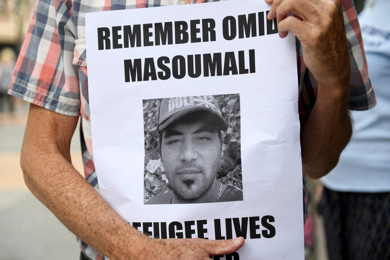 A photograph of Omid Masoumali is held outside the Brisbane magistrates court in 2019. The Iranian died after setting himself on fire at the Nauru detention centre in 2016.  (AAP Image/Dave Hunt)