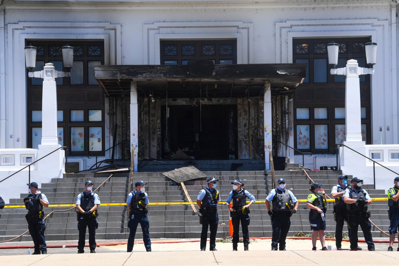 Police officers stand guard outside the fire damaged entrance to Old Parliament House in Canberra. (AAP Image/Lukas Coch) 