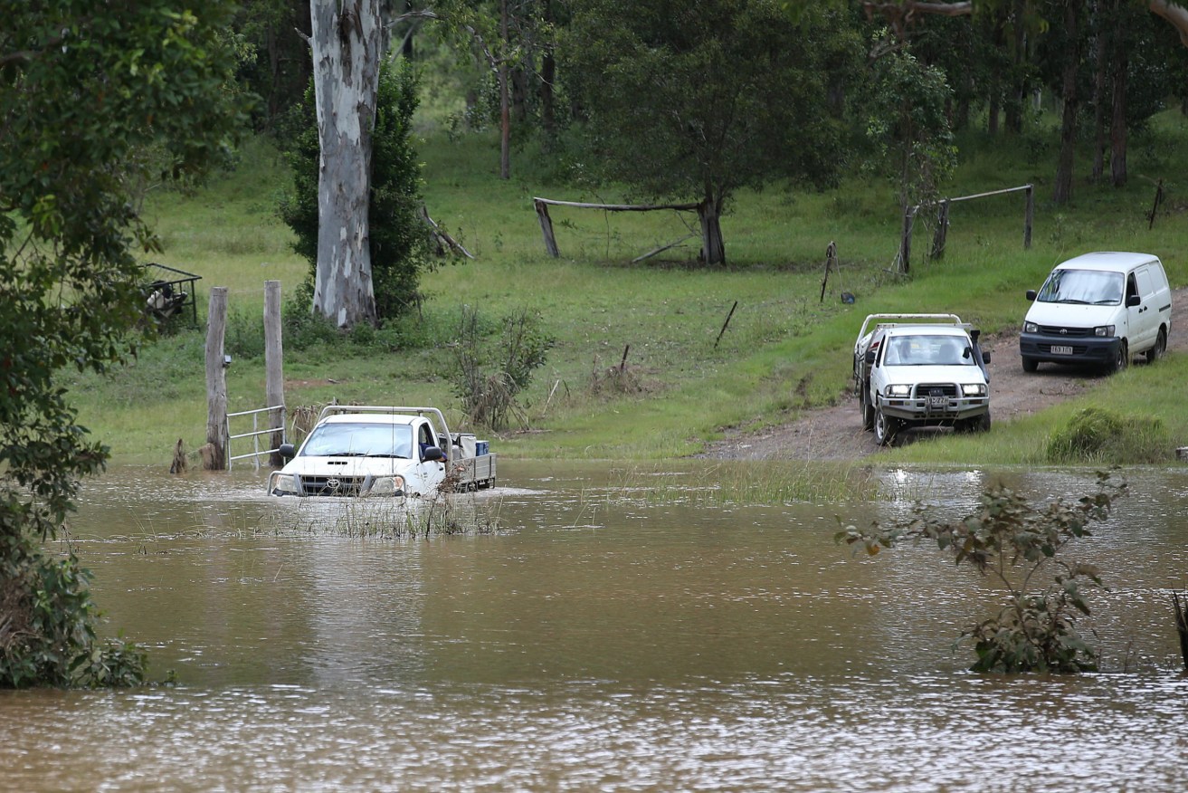 A car attempts to leave their flooded property but turns around near Belli Creek, on the Sunshine Coast. (AAP Image/Jono Searle)