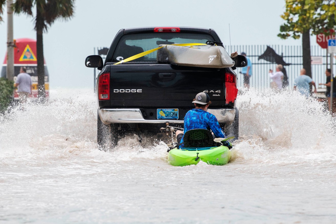 A truck pulls a man on a kayak on a low-lying road after flooding in aftermath of Hurricane Ian, in Key West, Fla. on a street near the Southernmost Point buoy. (AP Photo/Mary Martin)