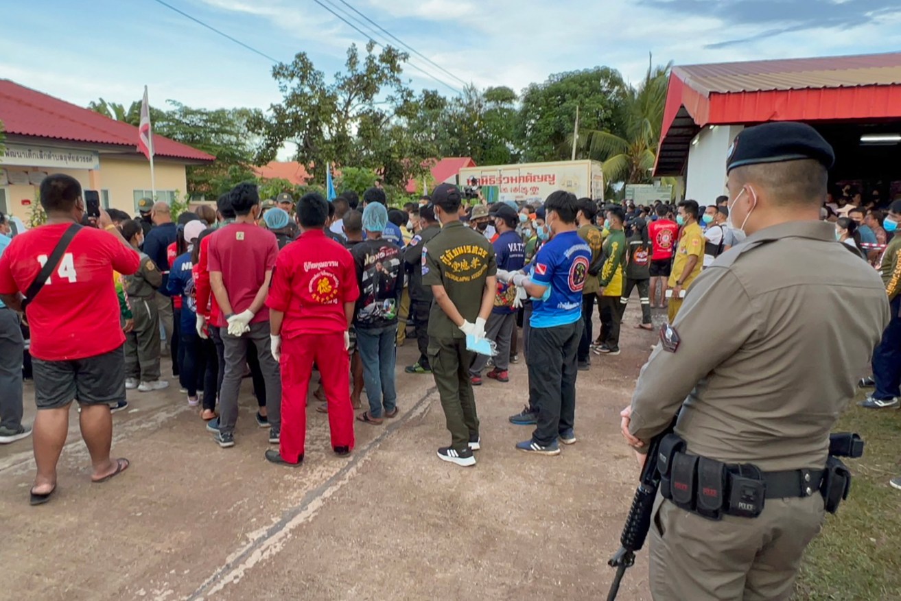 An armed police officer standing guard as rescue workers wait to collect the mass shooting victims' bodies while police investigate the crime scene at a childcare center in Nong Bua Lamphu province, northeastern Thailand. At least 35 people, mostly children, were killed when a former policeman carried out a mass shooting at a children care centre before killing himself, his wife and their child.  (EPA/RUAMKATANYU FOUNDATION)