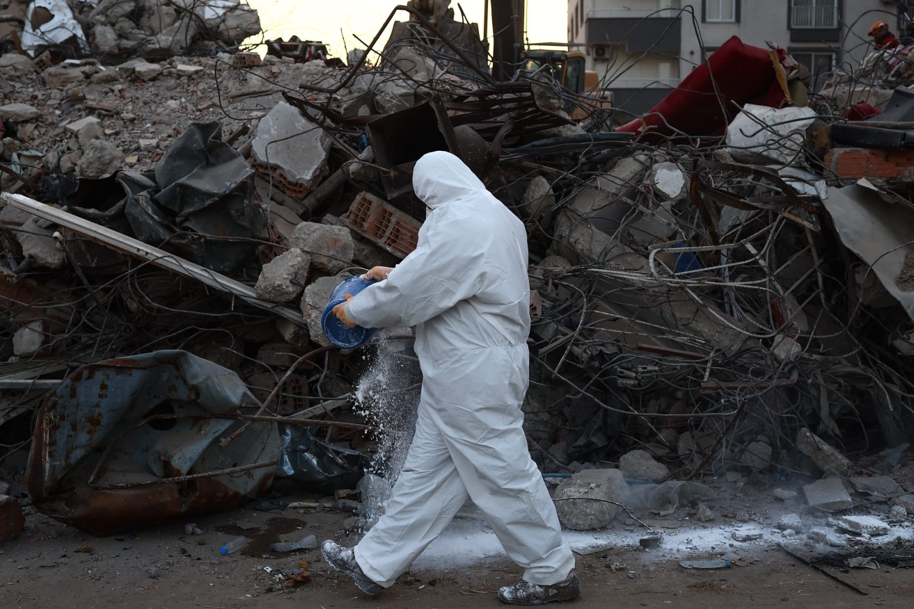 A Turkish soldier pours lime on debris to protect against infection and disease after a powerful earthquake in Hatay Turkey, 16 February 2023. (Image: EPA/SEDAT SUNA)