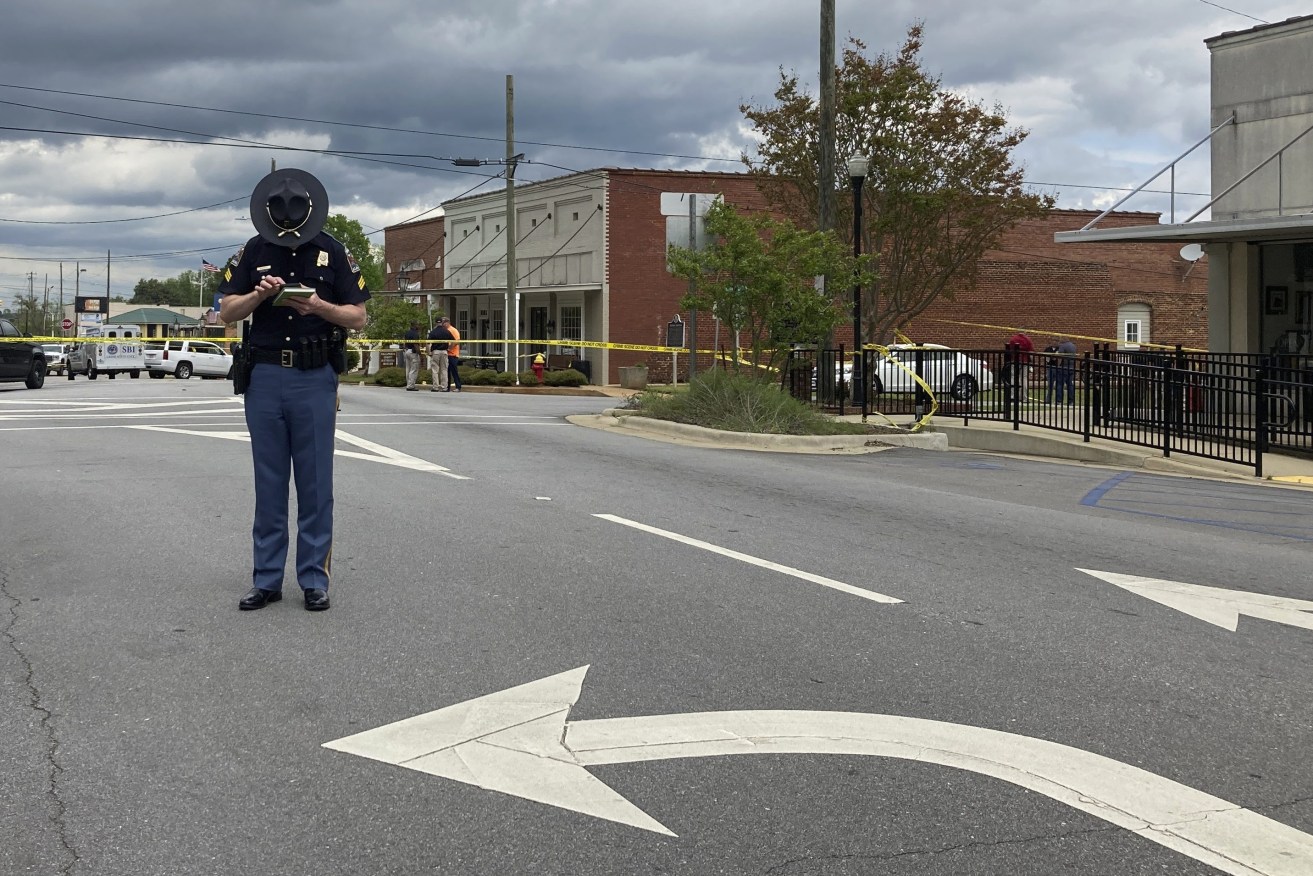 An Alabama state trooper checks his phone as investigators work at the site of a fatal shooting in downtown Dadeville, Ala., on Sunday, April 16, 2023. Several were killed during a shooting at a birthday party Saturday night, the Alabama Law Enforcement Agency said. (AP Photo/Jeff Amy)