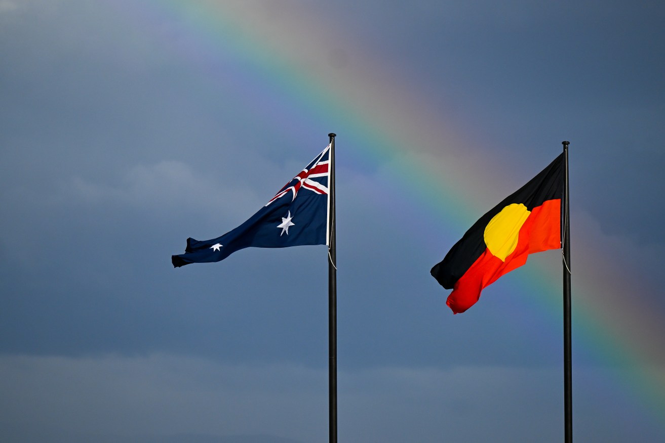 A rainbow is seen behind the Australian flag and the Indigenous flag in Canberra, Friday, July 28, 2023. (AAP Image/Lukas Coch) 