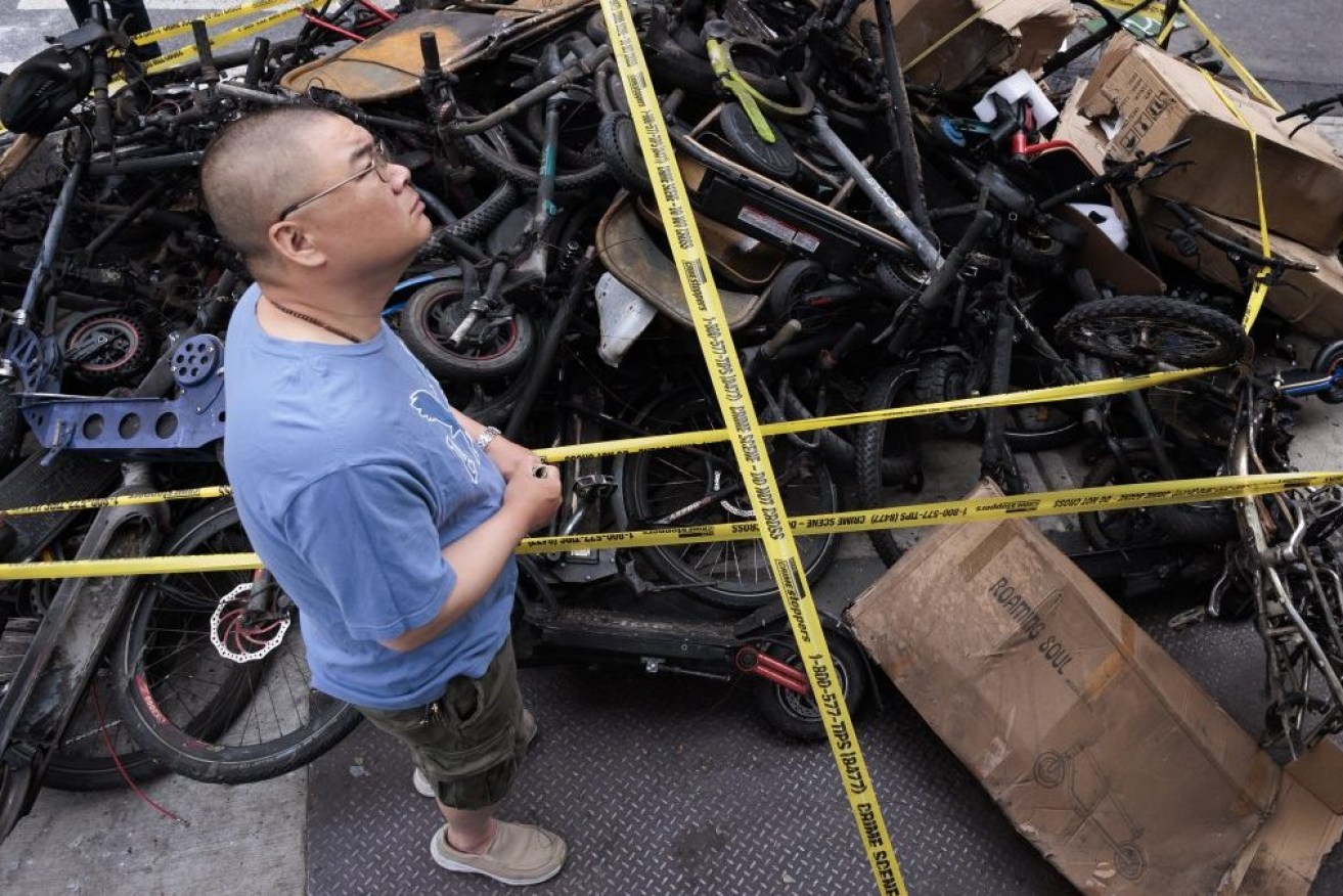 A man stands near a pile of burned e-bikes at the site of an overnight fire at an e-bike store that killed four people in the above apartment building in the Chinatown neighborhood of New York,  EPA/JUSTIN LANE