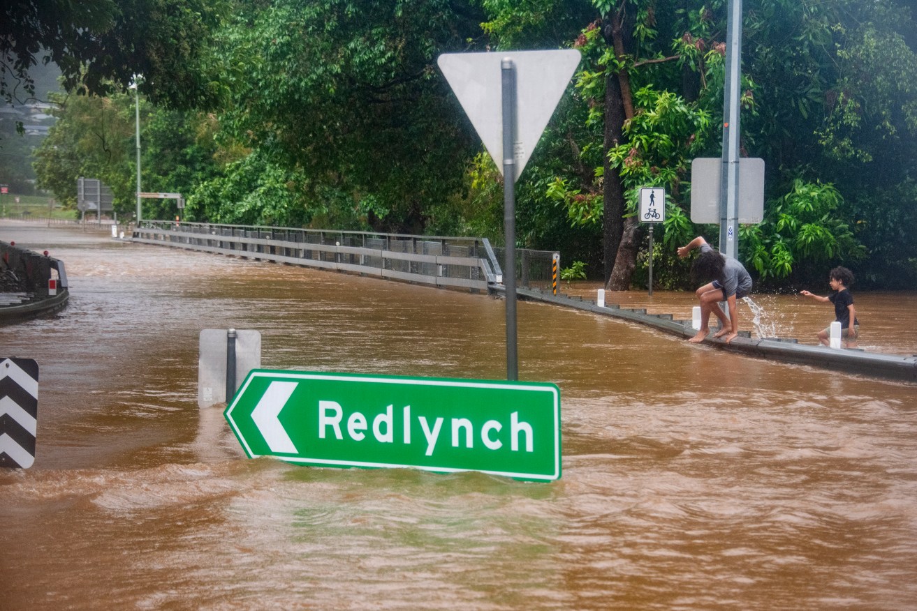 Children walk through flood waters near Redlynch in Cairns, Thursday, December 14, 2023. Cyclone Jasper has weakened to a tropical low but brought heavy rain and damaging winds, prompting people to be rescued in far north Queensland. (AAP Image/Brian Cassey) NO ARCHIVING